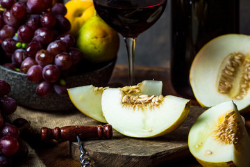 Bottle and glass of red wine, grape and cork on chair. Melon, piece of melon. Pink grape, pear. Still life of food. Dark food photography. Autumn concept. Alcohol, viticulture.