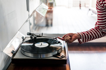 woman's hand dressed in red striped t-shirt putting a vinyl record on a record player inside a house