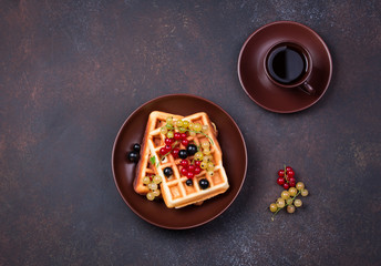 Plate of belgian waffles with currant berries on dark gray background. From top view