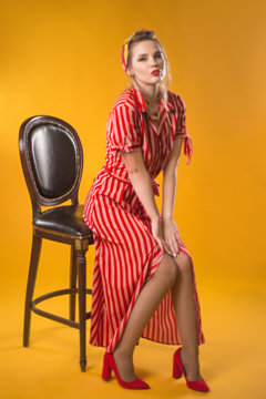 Girl in vintage style. In classic soft focus. Sits on a chair on a yellow background. In red striped