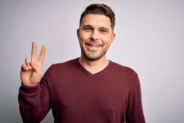 Naklejka premium Young man with blue eyes wearing casual sweater standing over isolated background smiling with happy face winking at the camera doing victory sign. Number two.