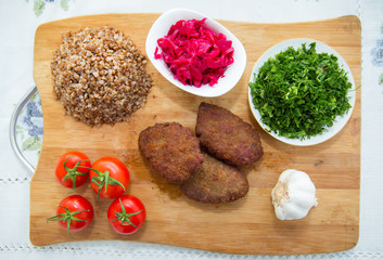 Meat cutlets, baked buckwheat on a wooden board . Red cabbage sauerkraut . Garlic, Onion, Tomatoes. Chopped coriander. Homemade cutlets with oatmeal on a wooden  . Meat cutlets on a wooden skewer .