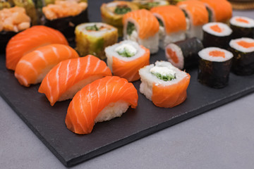 Set of sushi with wasabi, soy sauce and teapot on black stone background