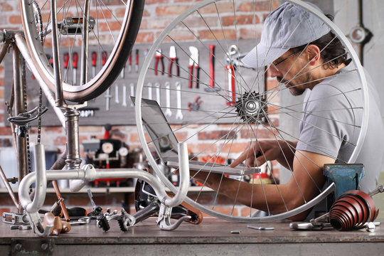 man repair the vintage bicycle at the computer search spare parts and see internet in garage workshop on the workbench with tools, diy concept - Powered by Adobe