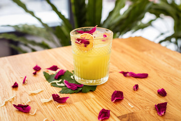 A refreshing citrus cocktail with ice in a rocks glass decorated with a dry orange slice and rose petals