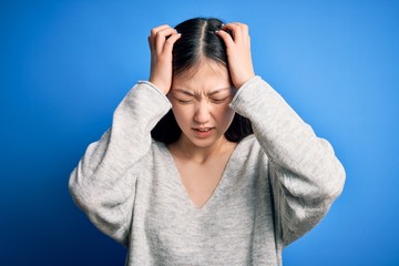 Young beautiful asian woman wearing casual sweater standing over blue isolated background suffering...