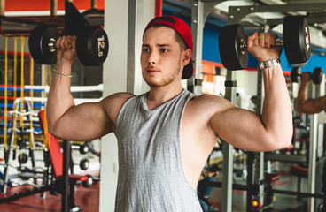 Fototapeta na wymiar Muscular young male athlete performs exercises with dumbbells. Strength training in the gym
