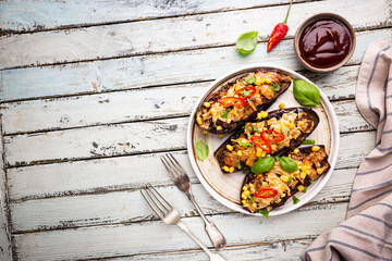 Baked aubergines boats, stuffed with minced meat, tomatoes, corn, garlic and cheese in white plate, top view