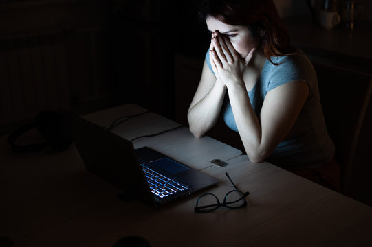 woman works overtime. A student studying at a laptop at night in the dark. The girl is worried about problems at work and holds her hands on her face.