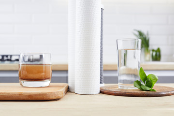 A glass of clean and dirty water with filter cartridges on the home kitchen background