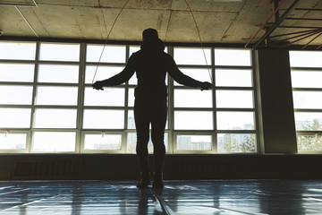 Silhouette of a man training and jumping rope in the gym in front of panoramic windows