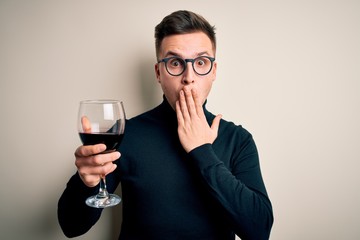 Young handsome caucasian man drinking an alcoholic glass of red wine over isolated background cover mouth with hand shocked with shame for mistake, expression of fear, scared in silence, secret