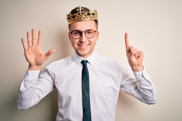 Young handsome caucasian business man wearing golden crown over isolated background showing and pointing up with fingers number six while smiling confident and happy.