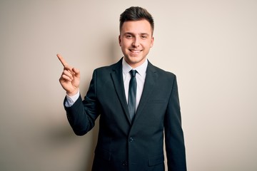 Young handsome business man wearing elegant suit and tie over isolated background with a big smile on face, pointing with hand finger to the side looking at the camera.