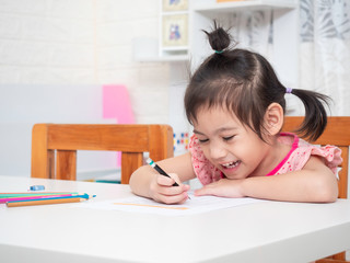 Asian little cute girl 4 years old learning to write alphabet at note on white table. Preschool...