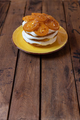 geschichtete Torte mit Quark, Sahne, Rührteig und kandierte Zitronenscheiben auf gelben Teller und braunen Tisch aus Holz