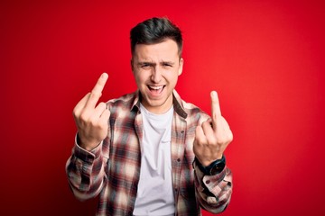 Young handsome caucasian man wearing casual modern shirt over red isolated background Showing middle finger doing fuck you bad expression, provocation and rude attitude. Screaming excited