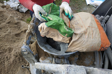 The worker mixes cement with sand in a concrete mixer.