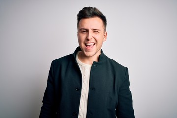 Young handsome business mas wearing elegant winter coat standing over isolated background winking looking at the camera with sexy expression, cheerful and happy face.