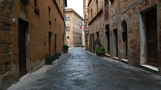 Smooth camera steady slide shot around old Tuscany village Pienza narrow empty streets, with old stone walls, shelled facades with flowers, early in the morning