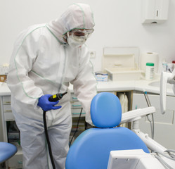 Doctor con traje de protección y desinfectando clinica dental