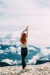A slender long-haired ginger girl stands on the top of a snowy mountain against the background of clouds. Back view, open space for your own text - 341040536