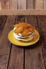 geschichtete Torte mit Quark, Sahne, Rührteig und kandierte Zitronenscheiben auf gelben Teller und braunen Tisch aus Holz