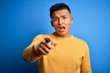 Young handsome latin man wearing yellow casual sweater over isolated blue background pointing displeased and frustrated to the camera, angry and furious with you