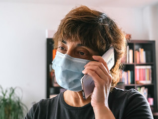 Woman alone in her home, protected by a mask against coronavirus, covid-19 or any other disease, talking on the phone from her living room