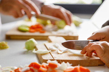 A girl's hands and her father cutting vegetables for cooking