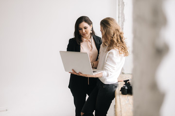 Two businesswomen work with laptop computer together against the window. Two business people working on laptop. Concept of teamwork young businessperson.