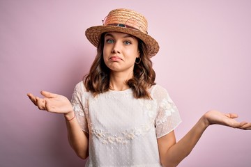 Young beautiful blonde girl wearing summer hat over pink isolated background clueless and confused...