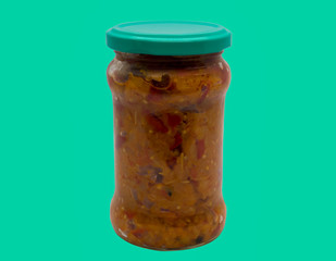 Traditional romanian mash vegetables (zacusca) in a glass jar on a green background.