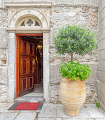 Fototapeta na wymiar old Greek orthodox church natural wood door on stone wall and potted plant