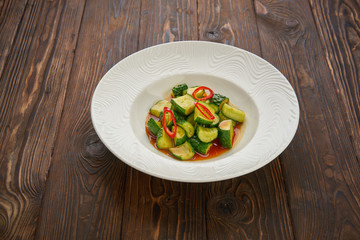 Chinese cucumber salad with chili pepper, garlic, soy sauce and sesame oil over wooden texture background. Asian beaten cucumber salad with chili and sesame seeds