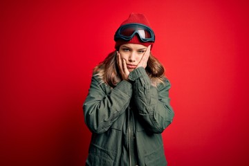 Young blonde girl wearing ski glasses and winter coat for ski weather over red background Tired hands covering face, depression and sadness, upset and irritated for problem
