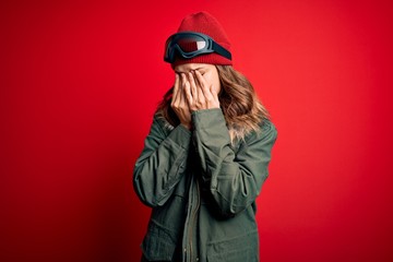 Young blonde girl wearing ski glasses and winter coat for ski weather over red background rubbing eyes for fatigue and headache, sleepy and tired expression. Vision problem