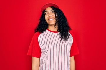 Young african american curly sportswoman wearing baseball cap and striped t-shirt looking away to side with smile on face, natural expression. Laughing confident.