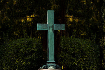 White christian green verdigrised cross in a graveyard with green foliage with copy space. Symbol for christianity, resurrection and Jesus Christ.