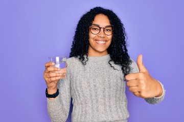 Young african american woman drinking glass of water over isolated purple background happy with big smile doing ok sign, thumb up with fingers, excellent sign