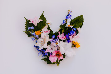 Wild flowers and leaves arranged in a heart shape on an off-white background in a flat lay style