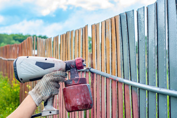 Painting metal fence spray. Man paints a fence with a paint sprayer. painting the fence to protect...