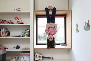 Ein Mädchen hängt während der Coronakrise gelangweilt kopfüber am Fenster am 01.04.2020.