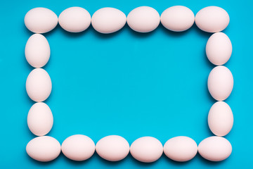 The original volumetric frame of white chicken eggs on a blue background. Top view. Copy space