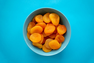 Dry apricots in turquoise bowl on blue background, top view. Heap of dried apricots.