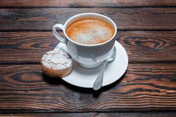 White cup of hot coffee with cookies on a plate on dark wooden board table background with blank copyspace in the big empty area for advertising text or ideas.
