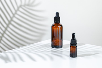 Creative photo of cosmetic bottle with pipette on a white background with shadow of tropical flower. Advertising