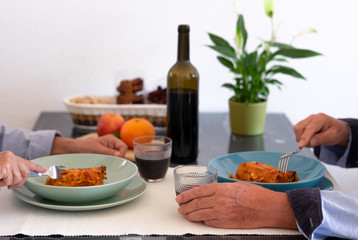Stay at home concept for coronavirus infection. Couple sitting at the table eating homemade Italian food. Pasta cannelloni stuffed with vegetables and meat sauce