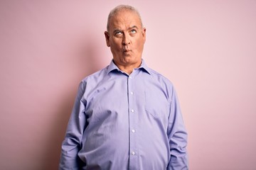 Middle age handsome hoary man wearing casual shirt standing over pink background making fish face with lips, crazy and comical gesture. Funny expression.