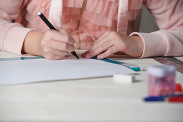 Girl in pink sweatshirt draws with black felt-tip pen at table. Blurred front background. Beige table